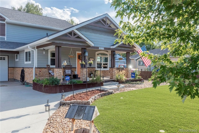 craftsman inspired home featuring a porch, a shingled roof, a front yard, stone siding, and driveway