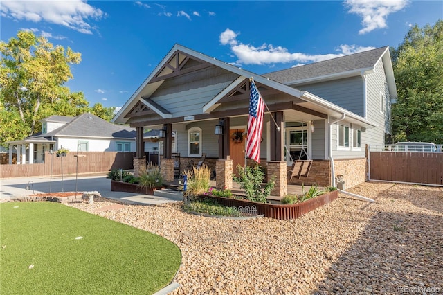 view of front of house featuring stone siding, fence, and a porch