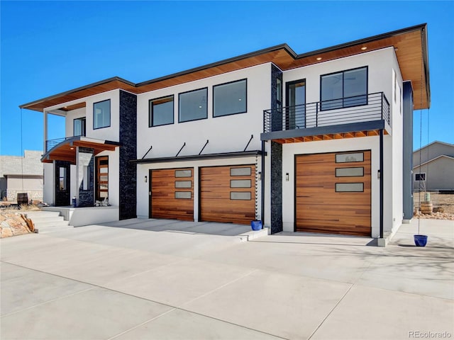 modern home with a balcony, an attached garage, driveway, and stucco siding