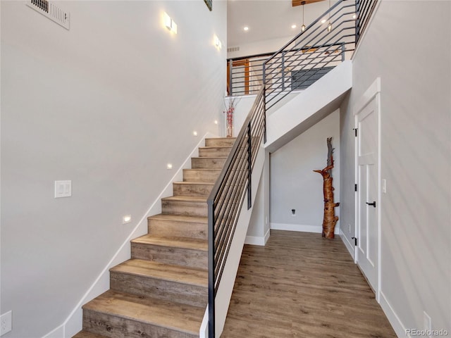 stairs with visible vents, a towering ceiling, baseboards, and wood finished floors