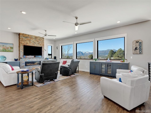 living area featuring beverage cooler, wood finished floors, a ceiling fan, recessed lighting, and a stone fireplace