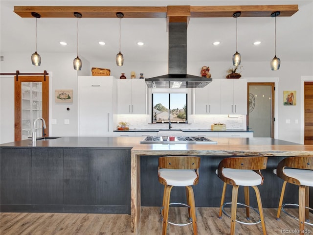 kitchen featuring island exhaust hood, a sink, white cabinetry, a barn door, and stainless steel gas cooktop