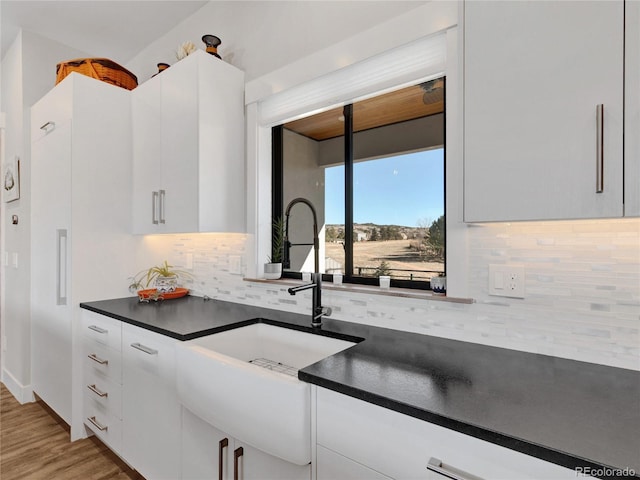 kitchen featuring tasteful backsplash, dark countertops, wood finished floors, and white cabinetry