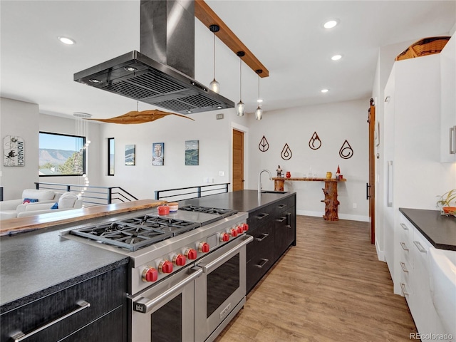 kitchen featuring double oven range, light wood-type flooring, dark countertops, wall chimney range hood, and dark cabinets