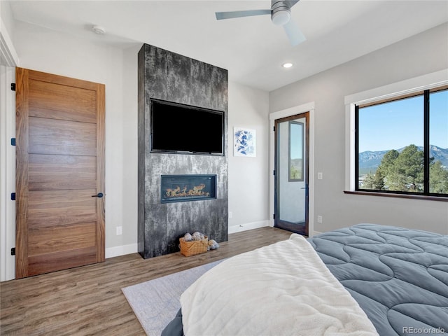 bedroom featuring wood finished floors, baseboards, recessed lighting, ceiling fan, and a tiled fireplace