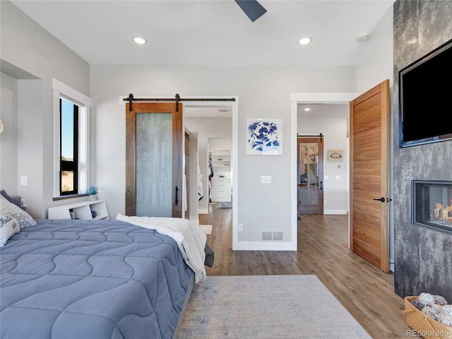 bedroom featuring visible vents, wood finished floors, recessed lighting, a barn door, and a large fireplace