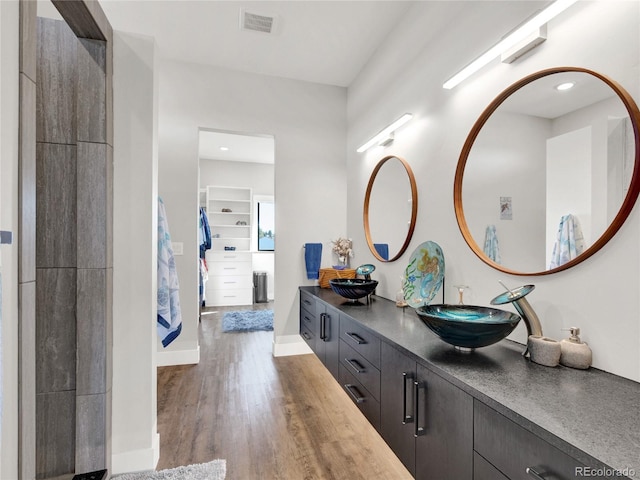 bathroom featuring visible vents, a sink, wood finished floors, double vanity, and baseboards