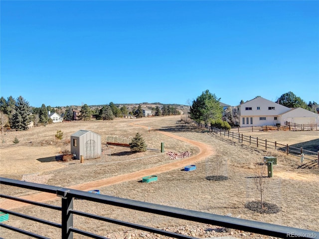 view of yard with an outbuilding, a rural view, a storage unit, and fence