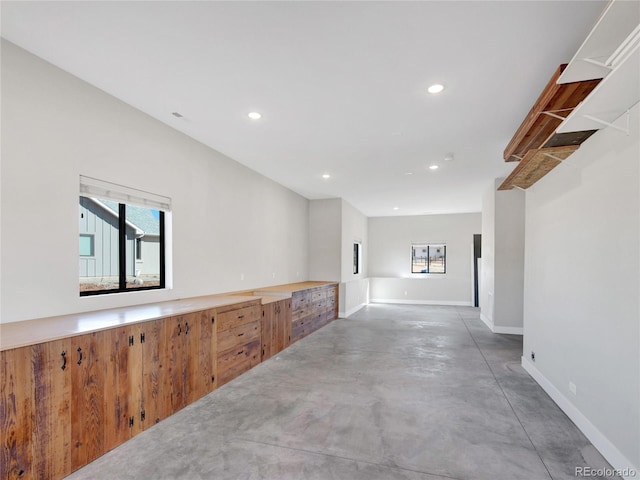 hallway with finished concrete floors, recessed lighting, and baseboards