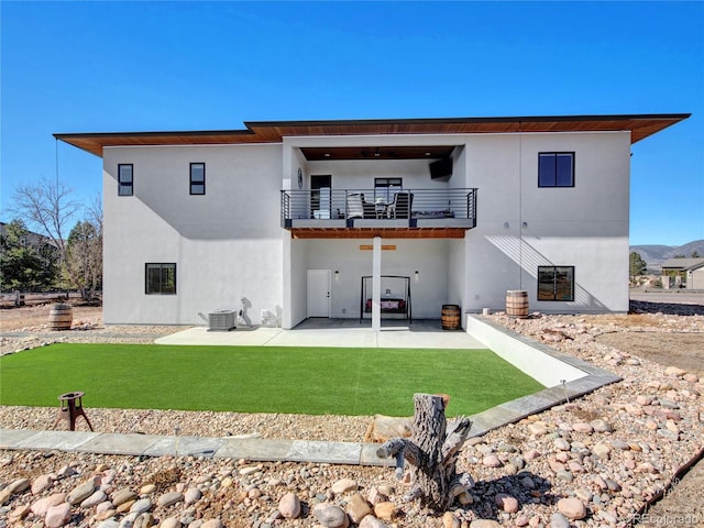 back of house with a balcony, cooling unit, stucco siding, a patio area, and a lawn