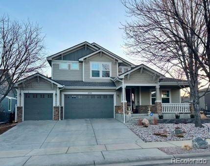 craftsman-style home with stone siding, a porch, concrete driveway, and a garage