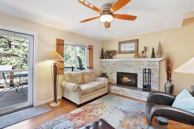 living area featuring ceiling fan, baseboards, a stone fireplace, and wood finished floors
