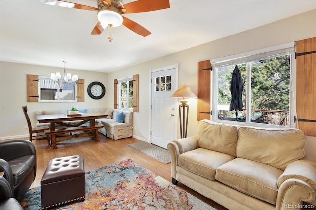 living area with ceiling fan with notable chandelier, baseboards, a healthy amount of sunlight, and wood finished floors