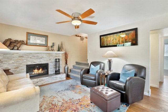 living area featuring wood finished floors, a fireplace, ceiling fan, stairway, and baseboards