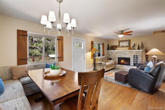 dining area with a fireplace, light wood-style flooring, ceiling fan with notable chandelier, and a healthy amount of sunlight