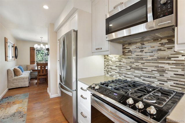 kitchen featuring baseboards, light wood finished floors, white cabinetry, a chandelier, and stainless steel appliances