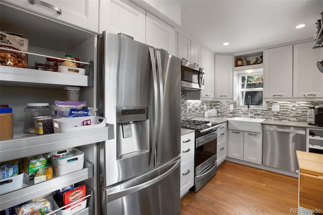kitchen featuring a sink, stainless steel appliances, open shelves, light countertops, and decorative backsplash