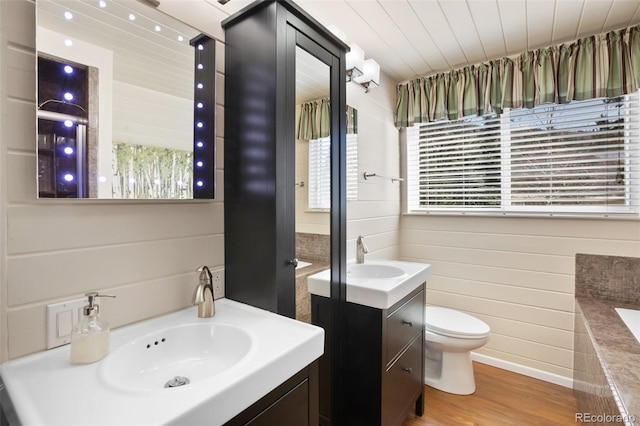 bathroom featuring toilet, wood finished floors, vanity, wooden walls, and a relaxing tiled tub