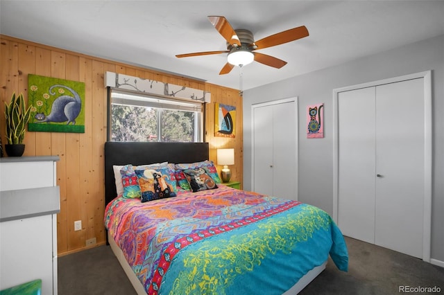 bedroom with multiple closets, carpet flooring, wooden walls, and ceiling fan