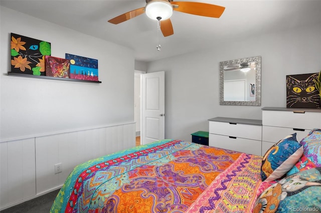 carpeted bedroom featuring wainscoting and a ceiling fan
