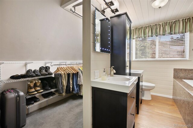 full bathroom with wood walls, toilet, wood finished floors, vanity, and tiled tub