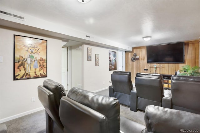 carpeted home theater room with visible vents, baseboards, and wooden walls