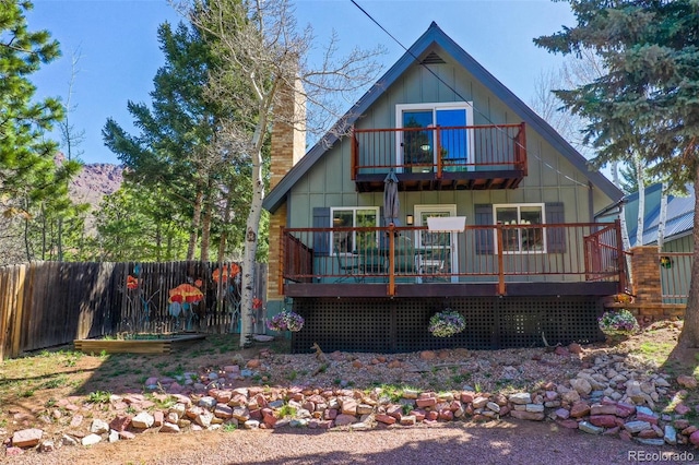 rear view of property featuring fence, a wooden deck, a chimney, and a balcony