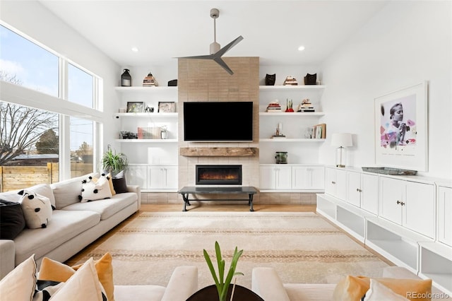 living room featuring built in features, a tile fireplace, and light wood-type flooring