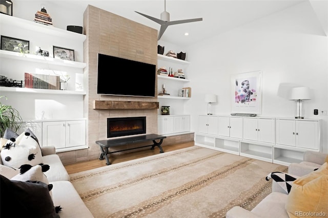 living room with a tile fireplace, hardwood / wood-style floors, built in features, and ceiling fan