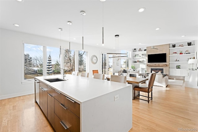 kitchen with sink, built in features, a large fireplace, an island with sink, and decorative light fixtures