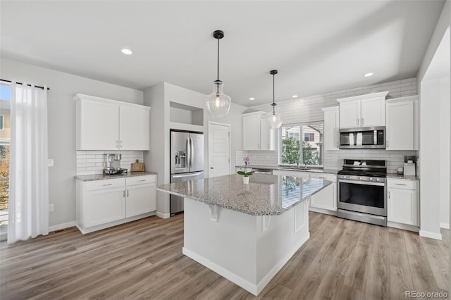 kitchen featuring appliances with stainless steel finishes, light wood finished floors, white cabinetry, decorative backsplash, and a kitchen island
