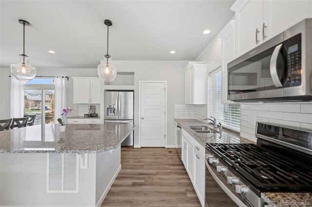 kitchen featuring decorative backsplash, a kitchen island, light wood-type flooring, a sink, and appliances with stainless steel finishes