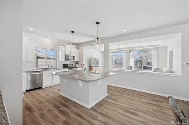 kitchen with light wood-style floors, a breakfast bar area, stainless steel appliances, white cabinetry, and decorative backsplash