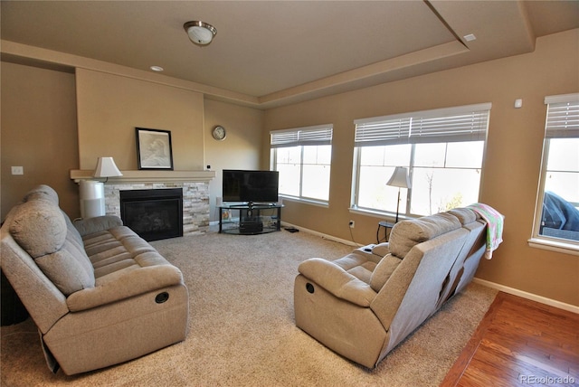 living area featuring baseboards, a tray ceiling, and a stone fireplace