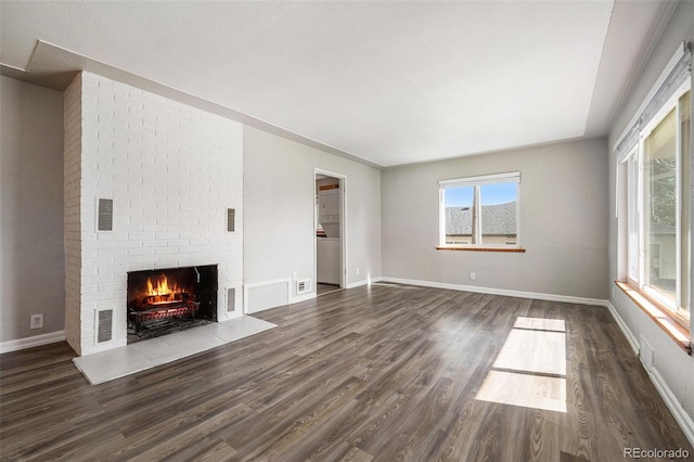 unfurnished living room with a brick fireplace and dark hardwood / wood-style floors