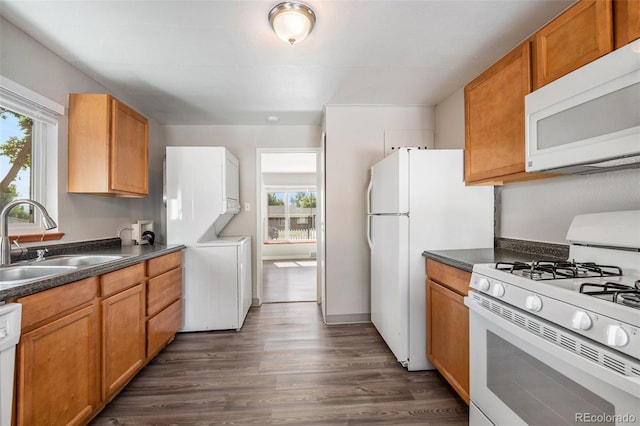 kitchen with white appliances, stacked washing maching and dryer, dark hardwood / wood-style flooring, and sink