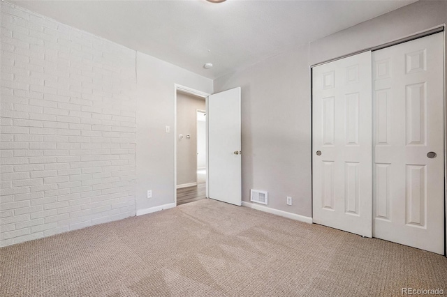 unfurnished bedroom with a closet, brick wall, and light carpet