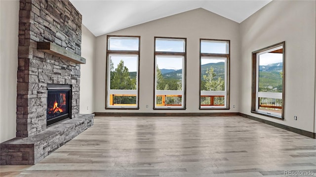 unfurnished living room with vaulted ceiling, a mountain view, hardwood / wood-style floors, and a fireplace