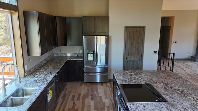 kitchen featuring sink, dark brown cabinets, appliances with stainless steel finishes, hardwood / wood-style flooring, and light stone countertops