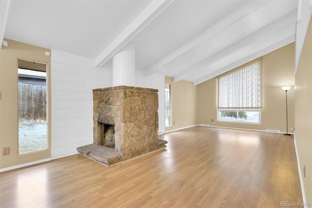 unfurnished living room with visible vents, vaulted ceiling with beams, baseboards, a stone fireplace, and wood finished floors