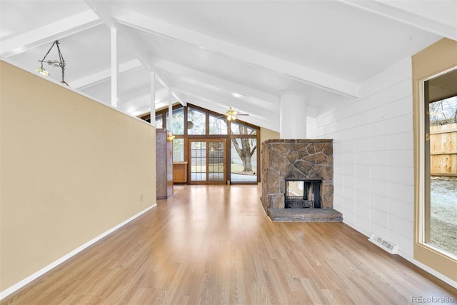 unfurnished living room with visible vents, lofted ceiling with beams, wood finished floors, a stone fireplace, and ceiling fan