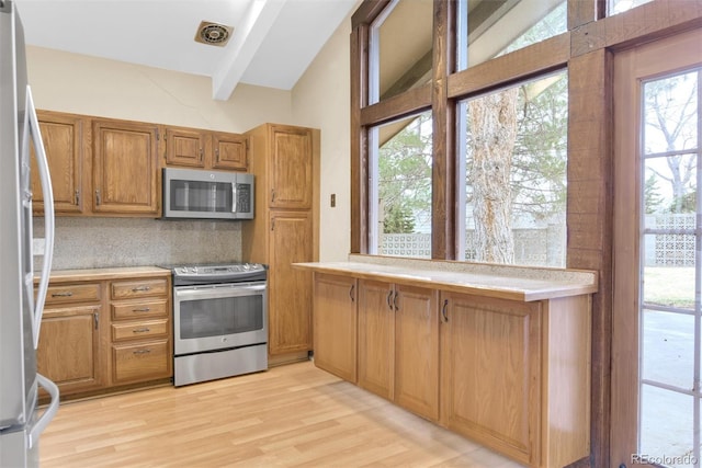 kitchen featuring backsplash, light countertops, vaulted ceiling with beams, and appliances with stainless steel finishes