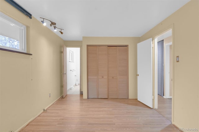 unfurnished bedroom with light wood finished floors, rail lighting, and a closet