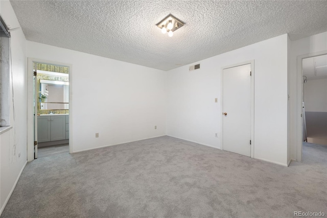 unfurnished bedroom featuring ensuite bathroom, a textured ceiling, and light carpet