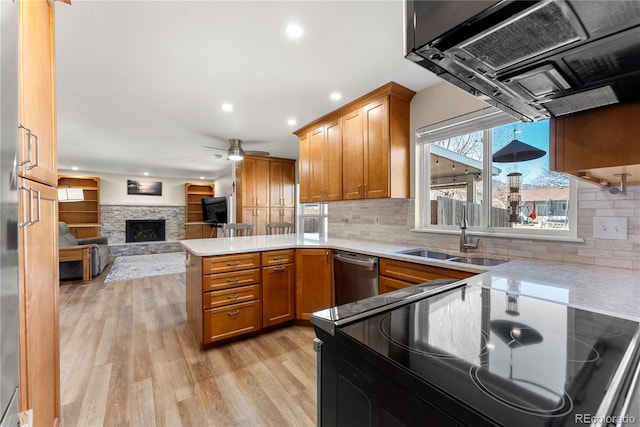 kitchen with a sink, stainless steel dishwasher, a peninsula, a stone fireplace, and brown cabinetry