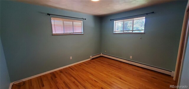 unfurnished room with a baseboard radiator, baseboards, and wood finished floors