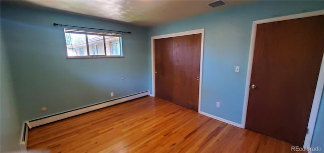 unfurnished bedroom featuring a closet, visible vents, wood finished floors, and a baseboard radiator