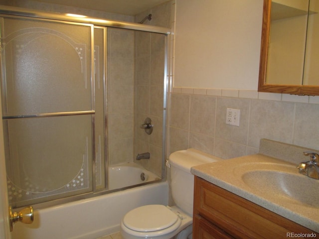 bathroom featuring vanity, toilet, tile walls, and bath / shower combo with glass door