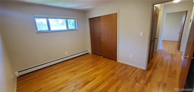 unfurnished bedroom with a baseboard heating unit, baseboards, light wood-style floors, and a closet