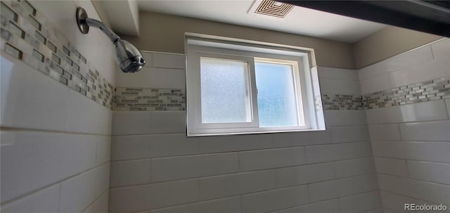 full bath featuring visible vents and tiled shower